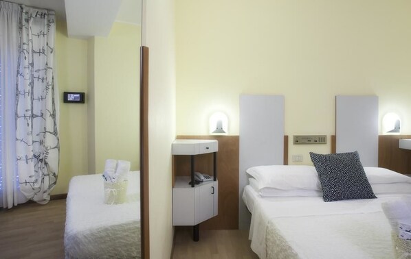 A hotel room with two beds, a bedside table with a phone, a lamp, and a small basket with towels. - Hotel Bel Air (Riccione)