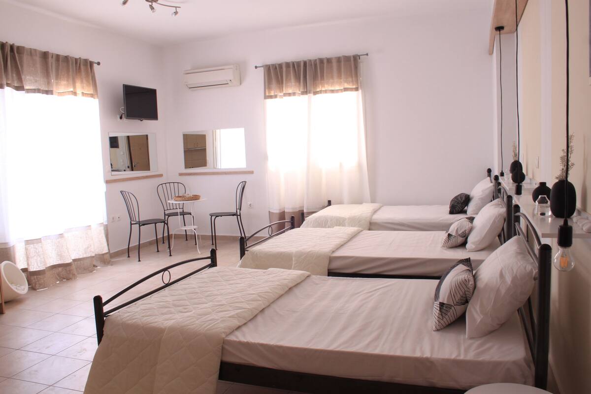 A hotel room with three beds, a desk, chairs, and a TV.