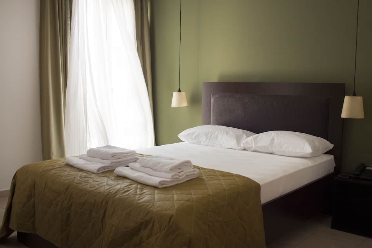 A neatly made bed with folded towels, a headboard, and two bedside lamps.