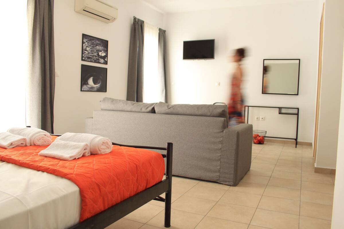 A modern hotel room with a bed, a sofa, a flat-screen TV, and a mirror.