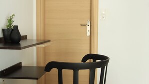 A room with a wooden door, a black chair, and a shelf with a plant. - Krinis Apartments (Rhodes)