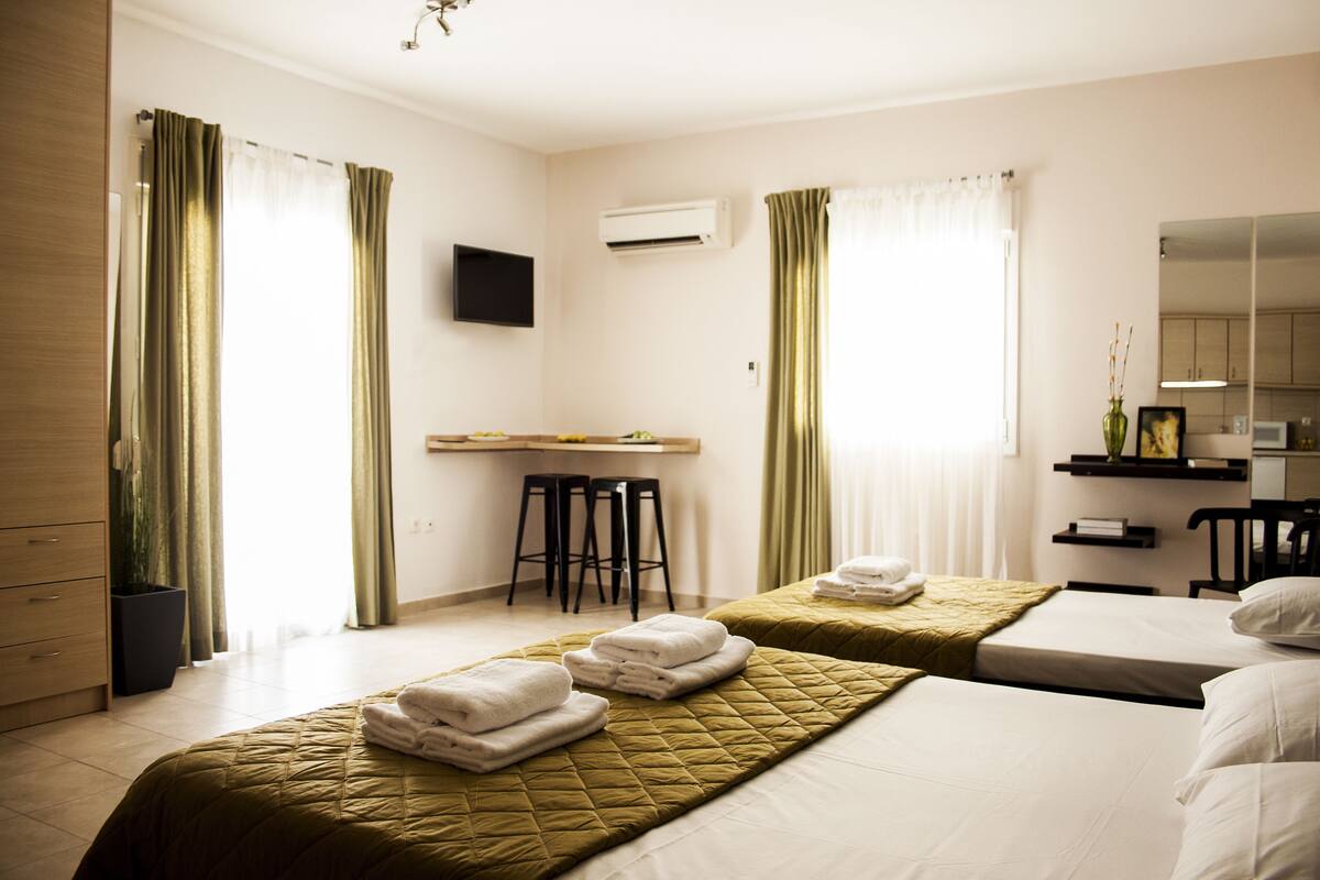 A hotel room with two beds, a desk with stools, a TV, and a mirror.