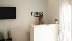 A modern reception area with a flat-screen TV mounted on the wall, a reception desk, and a potted plant. - Krinis Apartments (Rhodes)