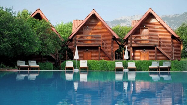 Um hotel tipo cabana de madeira, com piscina, cadeiras de descanso e escadaria que leva ao terraço.