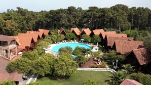 Um resort com várias cabanas, uma piscina central e vegetação ao redor.