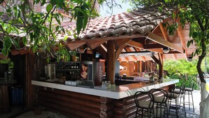 Uma área de bar com balcão de madeira, teto de telhas e banquetas.