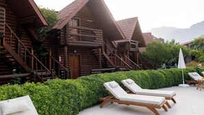 Um hotel em estilo cabana de tronco com varandas de madeira, área de piscina com espreguiçadeiras e um jardim bem cuidado.