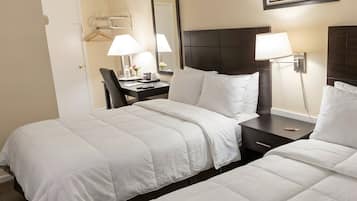 A hotel room with two beds, a desk, a chair, a lamp, and a framed picture on the wall.