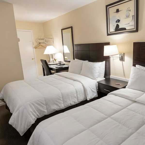 A hotel room with two beds, a desk, a chair, a lamp, and a framed picture on the wall. - North Star Motel (Shelburne)