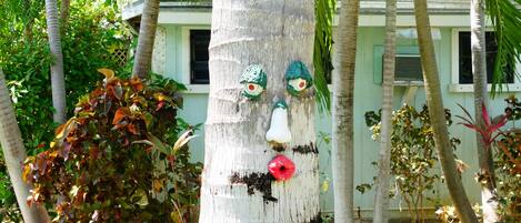 A tree with painted faces and lips, surrounded by greenery and a building in the background.