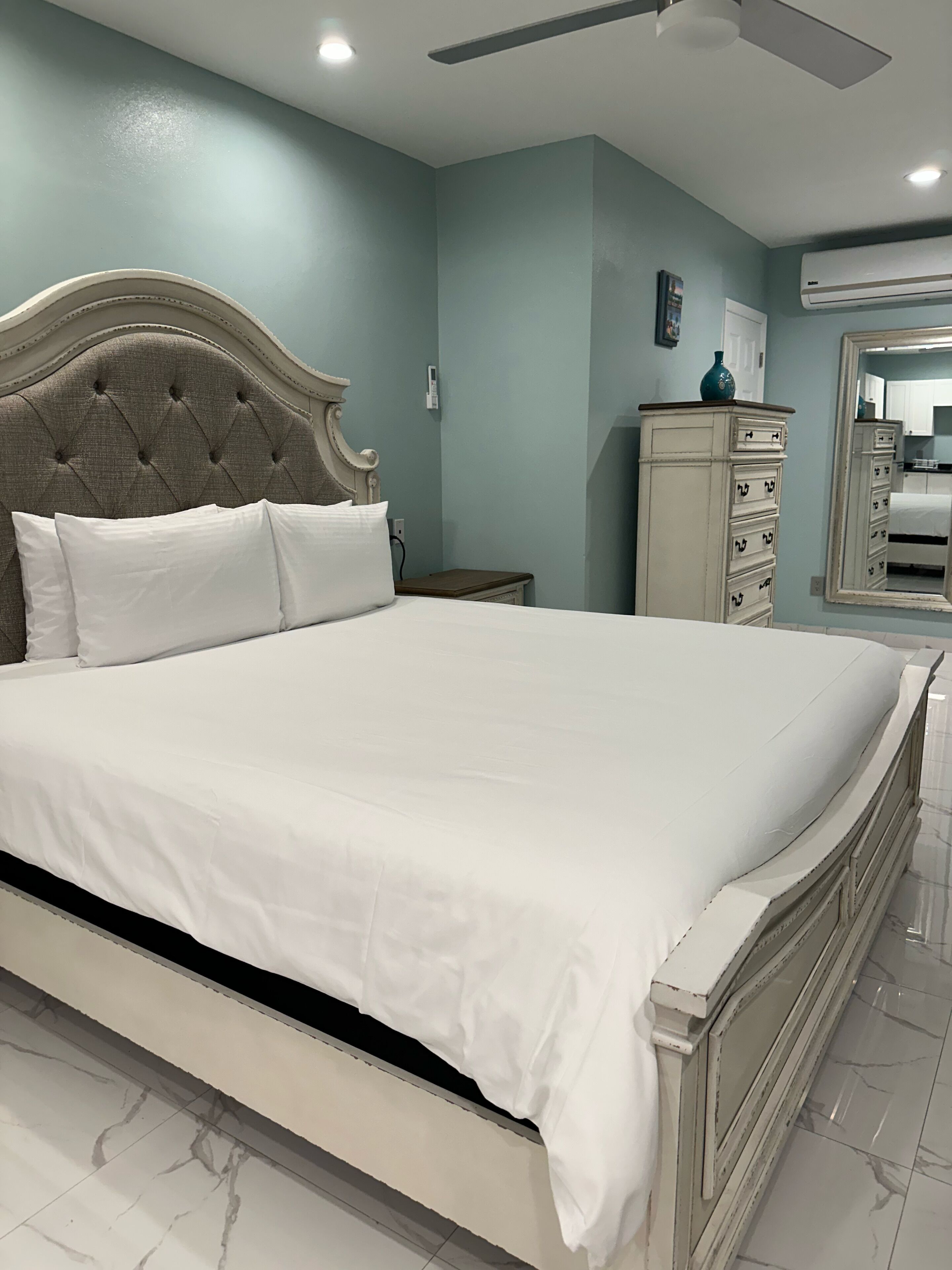 Une chambre à coucher avec un grand lit, une table de chevet, une commode et un ventilateur de plafond.