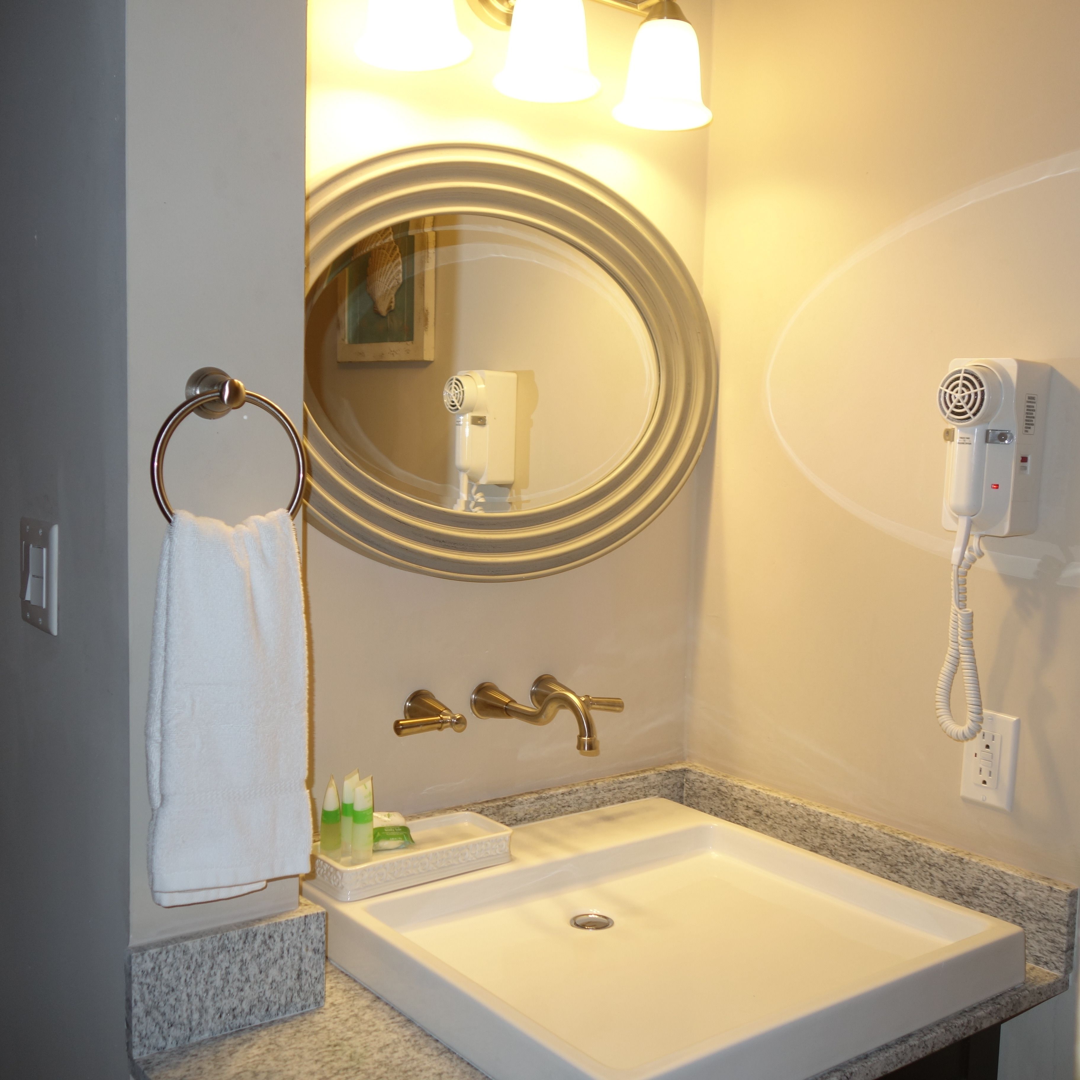 Un baño con lavabo, espejo, toallero y secador de pelo montado en la pared.