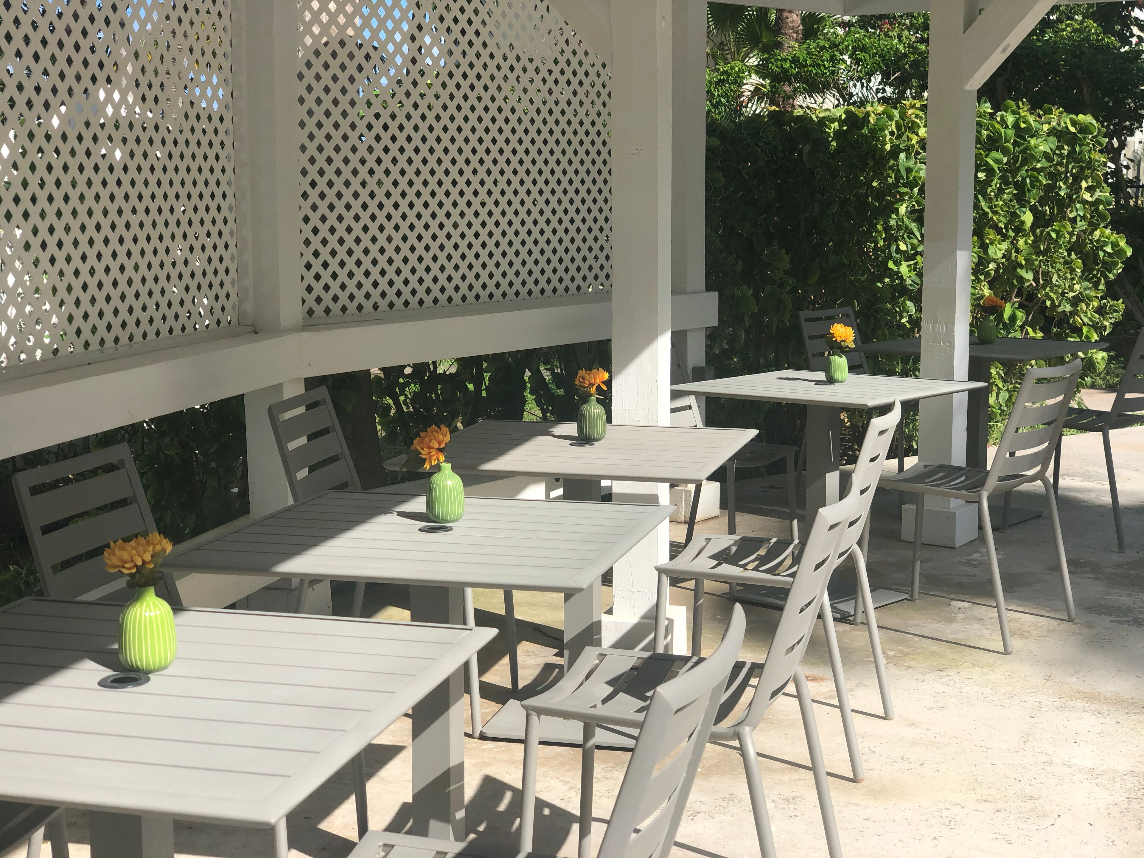 An outdoor patio area with white tables and chairs, some with vases of flowers.