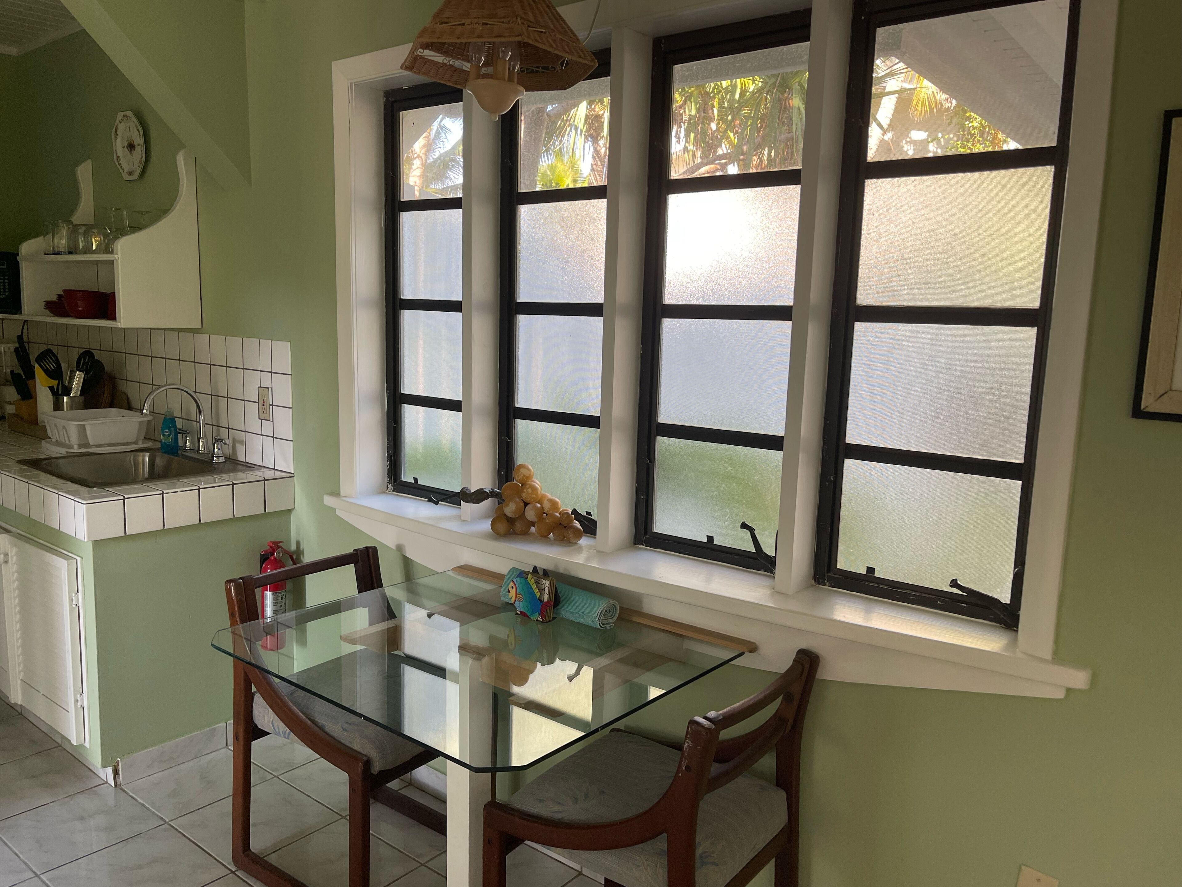 A kitchen with a glass table and chairs, a sink, and a window with frosted glass panes.