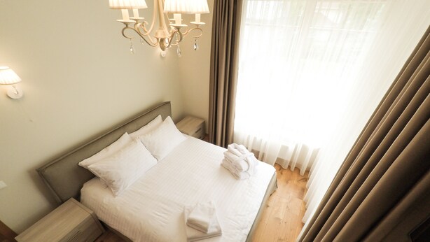 Un letto rifatto con lenzuola bianche, una testiera in legno e un comodino con una lampada.