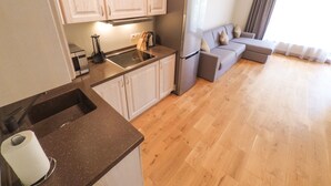 Una cucina moderna con piano cottura integrato, lavello e frigorifero, adiacente a un soggiorno con divano e una grande finestra.