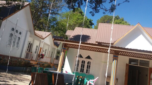 A traditional building with a tiled roof, a balcony with chairs, and a table. - Hostel Roma Inn 2 (Kalaw)