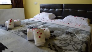 Ein ordentlich bezogenes Bett mit floraler Bettwäsche und einem Kopfteil, Handtücher mit roten Blumen, und ein Fenster mit Vorhängen.