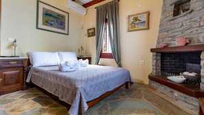 A bedroom with a stone floor, a bed with a patterned bedspread, a dresser, a fireplace with decorative items, and two framed paintings on the walls. - Green Island Resort Kea (Kea)