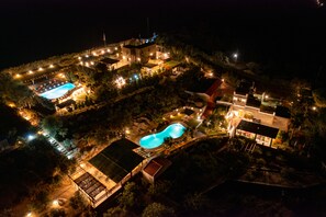 Luchtbeeld van een resort met meerdere zwembaden, verlichte paden en diverse gebouwen.