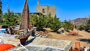 A model sailboat on a stone surface, a stone building in the background, and outdoor seating area with tables and chairs. - Green Island Resort Kea (Kea)