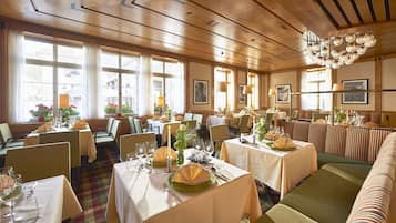 Ein Restaurant mit mehreren Tischen und Sitzecken, Holzboden und großen Fenstern.