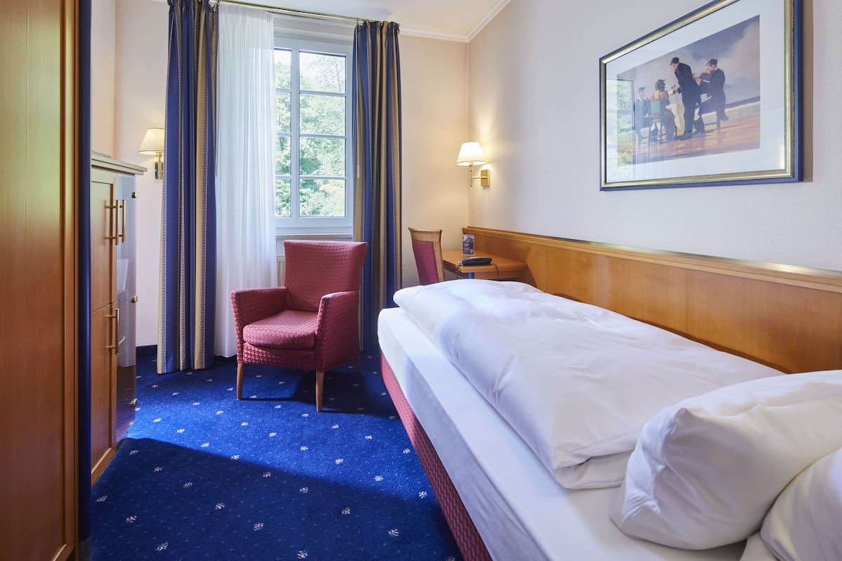 A hotel room with a bed, a chair, a desk, a lamp, and a window with curtains.