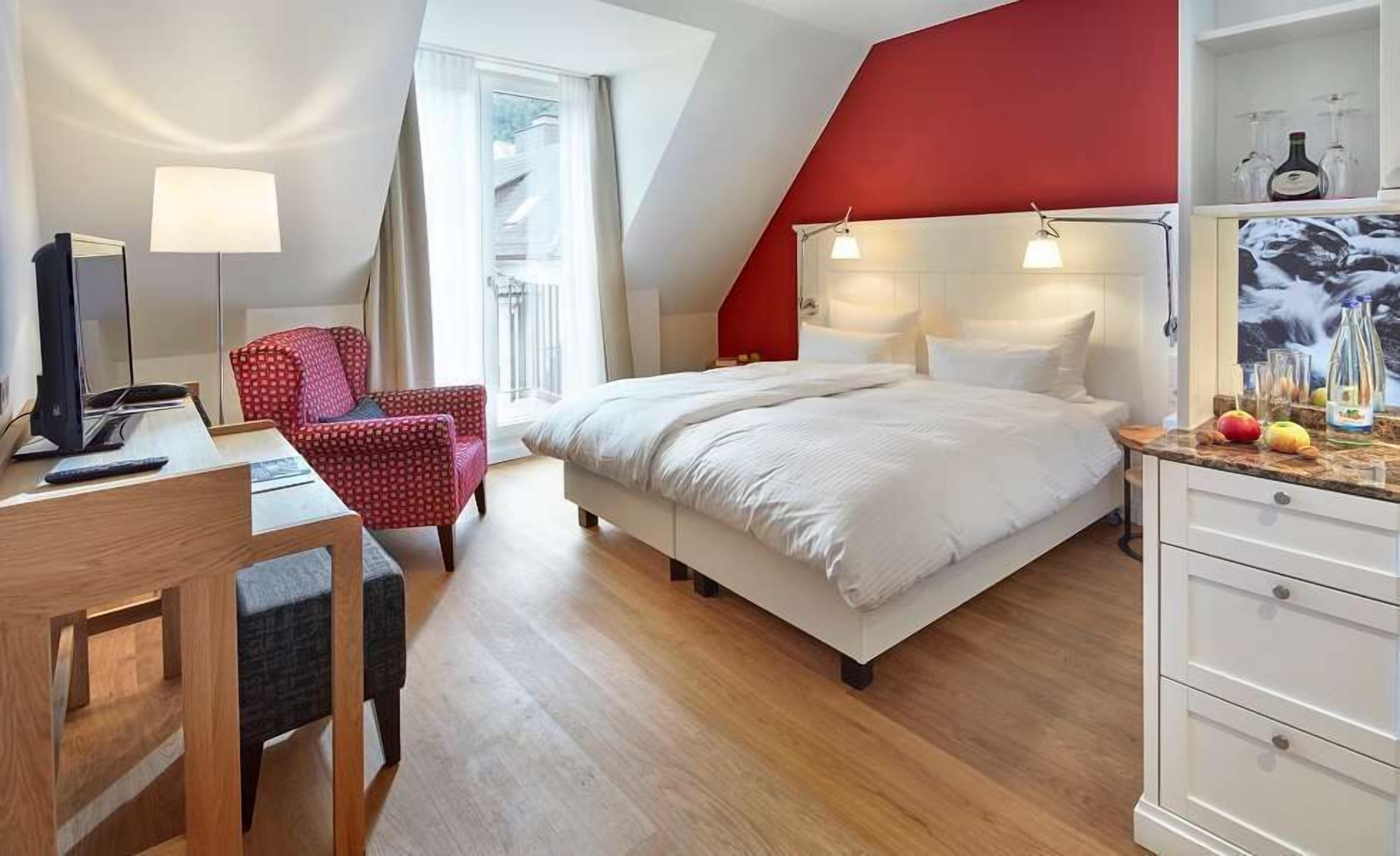Een slaapkamer met een bed, een bureau, een stoel, een televisie en een rode accentmuur.