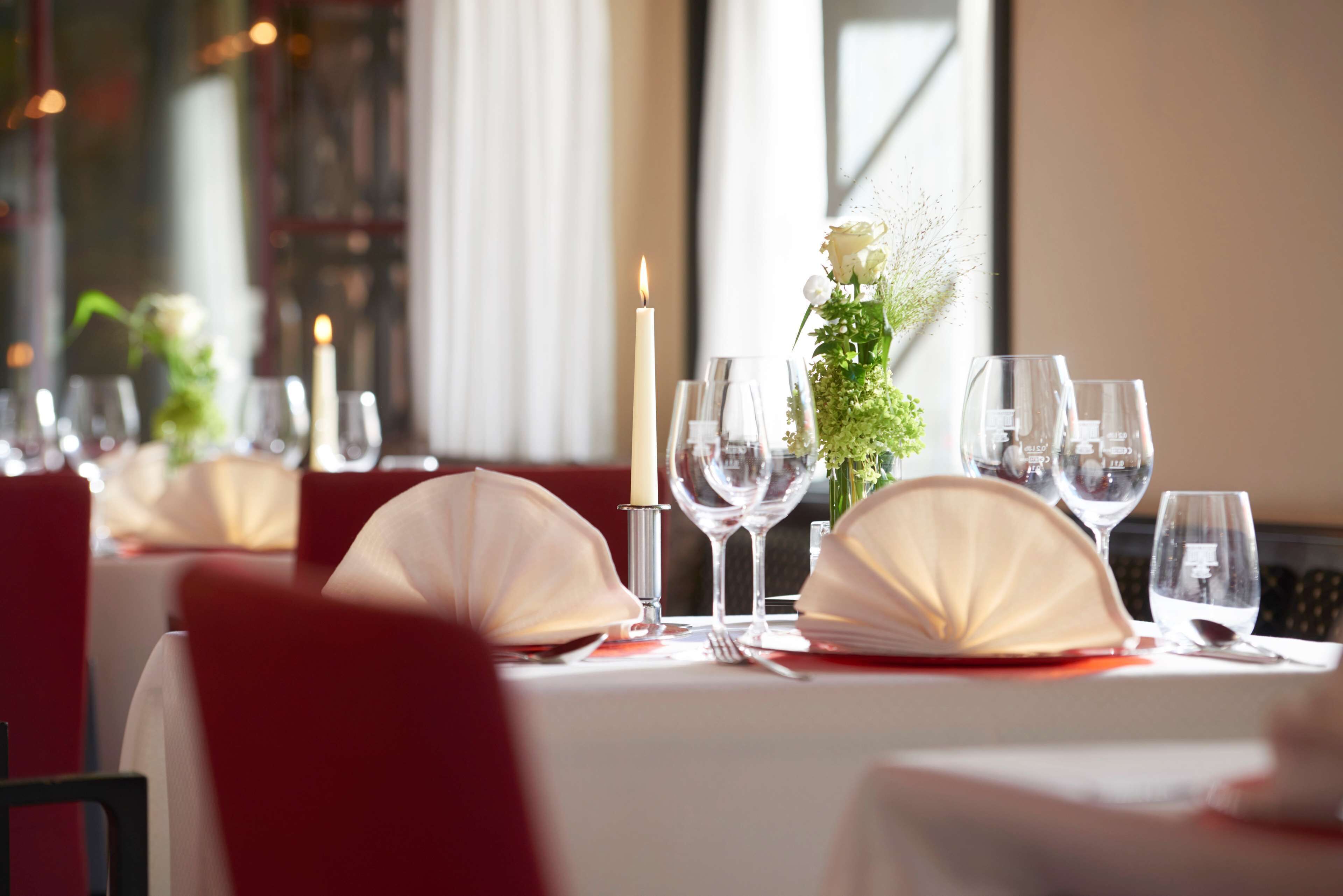 A dining table set with white tablecloths, red chairs, and a candle centerpiece.
