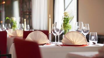 A dining table set with white tablecloths, red chairs, and a candle centerpiece.