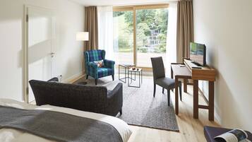 A hotel room with a bed, a desk with a computer, a chair, a sofa, and a view of a waterfall.