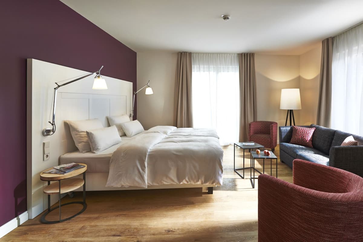 A hotel room with a bed, a desk, a chair, a sofa, and a lamp.