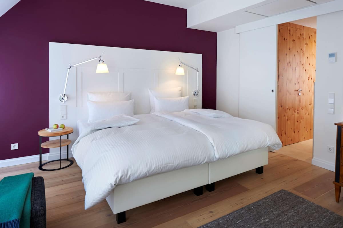 A modern bedroom with a large bed, two bedside lamps, a wooden dresser, and a wooden door.