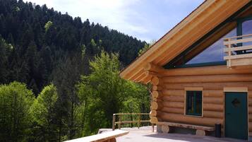 A wooden cabin with a bench and a view of a forested mountain.