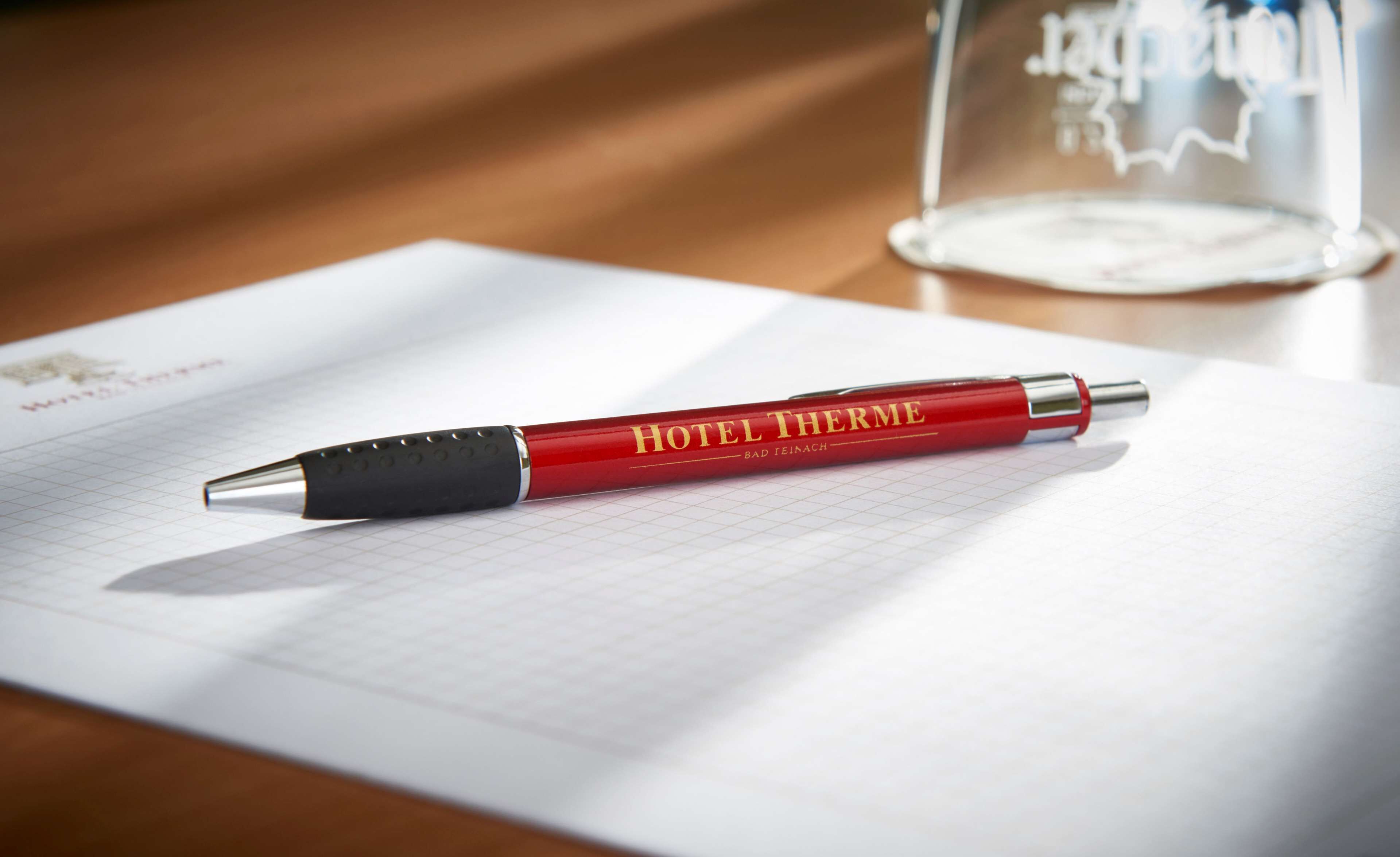 Una penna rossa con la scritta "HOTEL THERME" posata su un foglio di carta millimetrata.