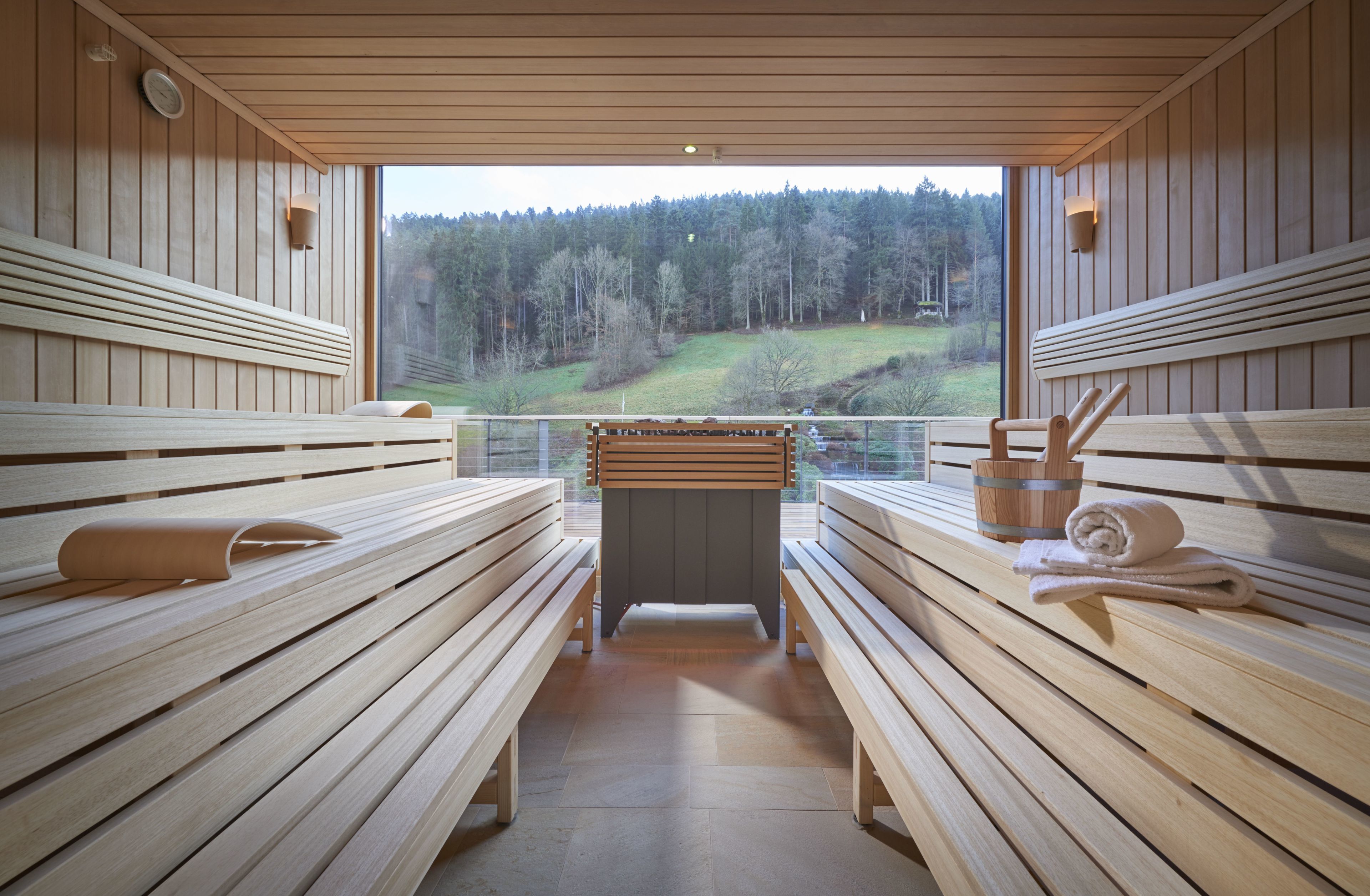 A sauna with wooden benches and a view of a forested landscape.
