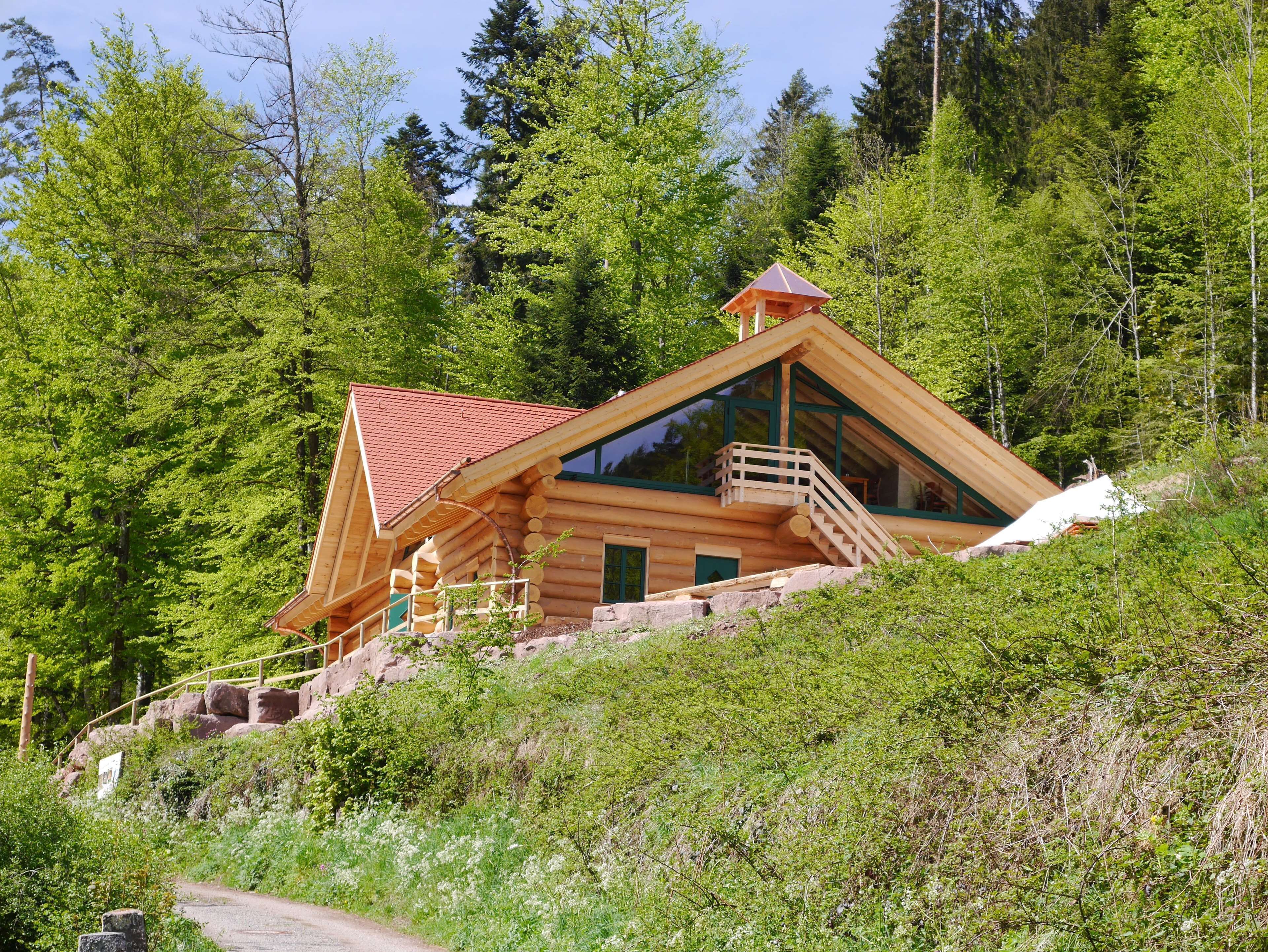 A log cabin with a red roof, a balcony, and a staircase leading to the entrance.