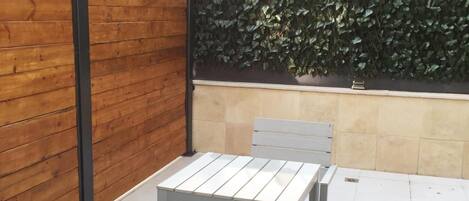 Un patio al aire libre con dos mesas y sillas de metal blanco, una valla de madera y una pared cubierta de follaje verde.