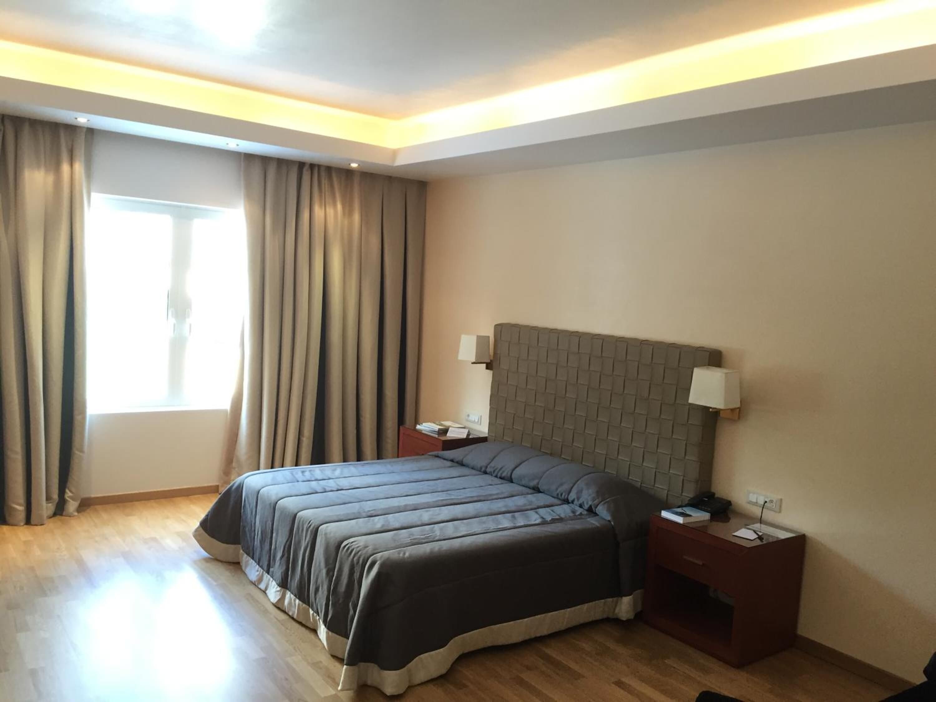 A modern hotel room with a large bed, wooden flooring, and a window with curtains.