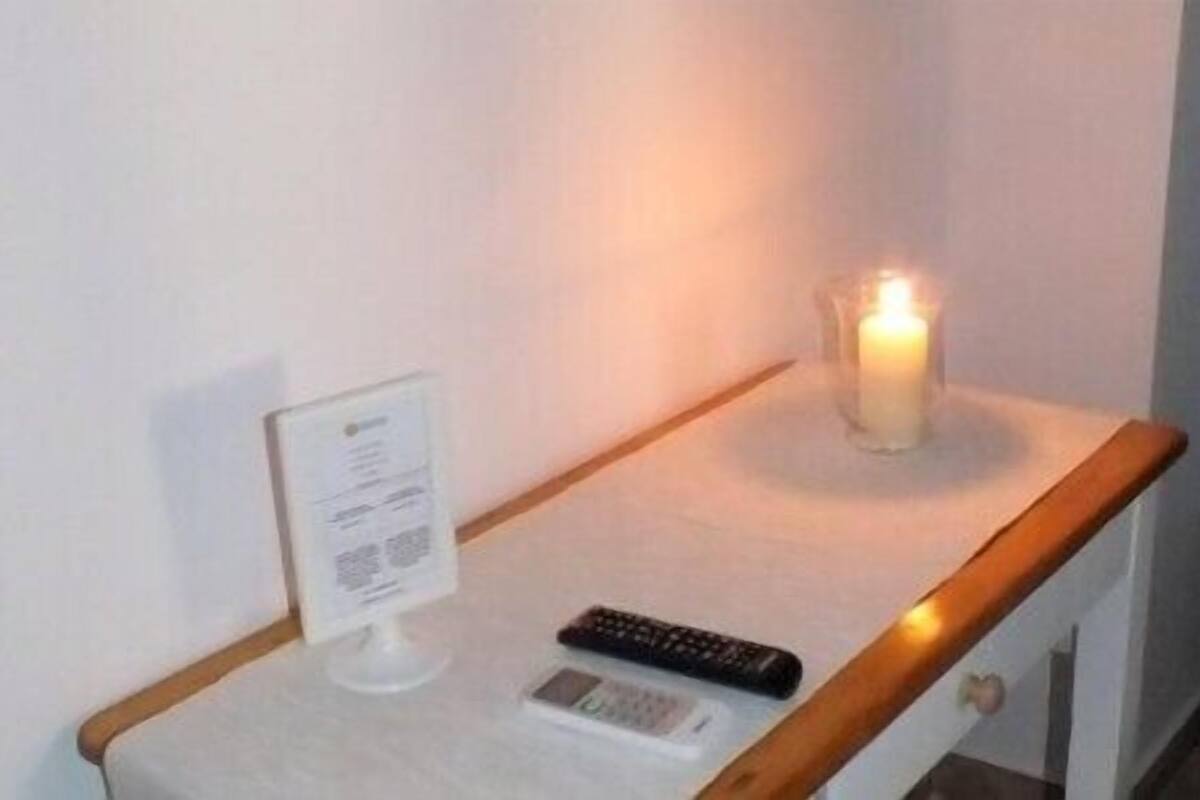 Une petite table avec une télécommande, une bougie et un panneau sur un mur blanc.
