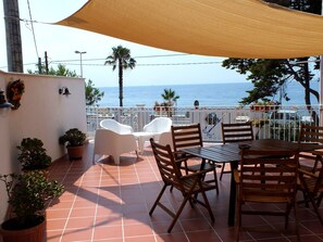 A terrace with a table and chairs, potted plants, and a view of the sea. - B&B Villa sul Mare (Melito di Porto Salvo)