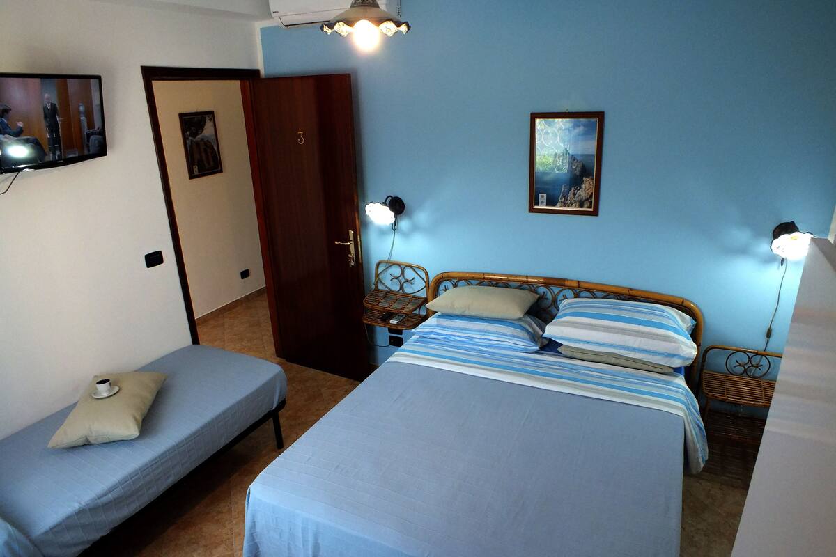 Une chambre avec deux lits simples, un lit double, une porte, un téléviseur fixé au mur et un tableau.