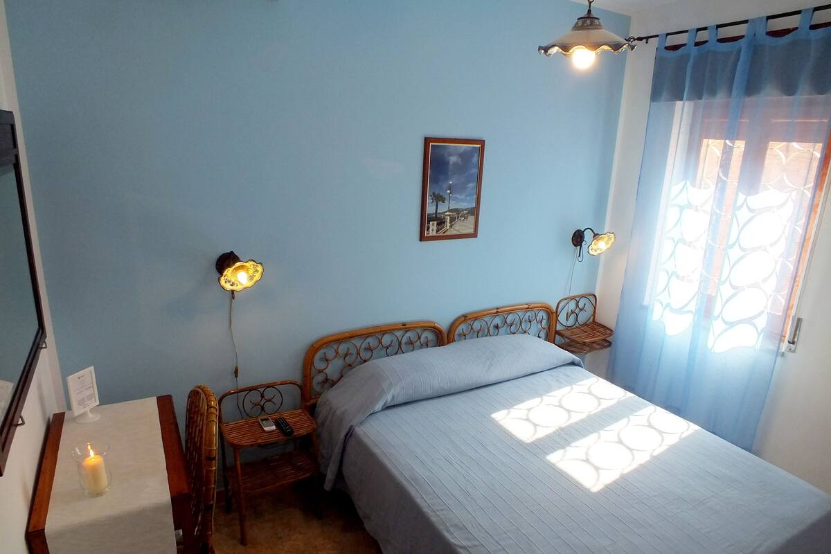 Une chambre à coucher avec un lit, une table de chevet, une table avec une bougie et une lampe fixée au mur.