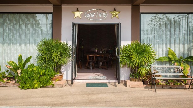 A building entrance with a sign above the door, potted plants, and a bench outside. - The Star Hotel (Udon Thani)