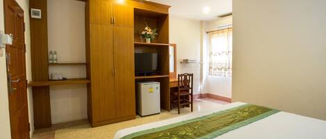 A bedroom with a bed, a wooden wardrobe, a small refrigerator, a television, and a desk with a chair.