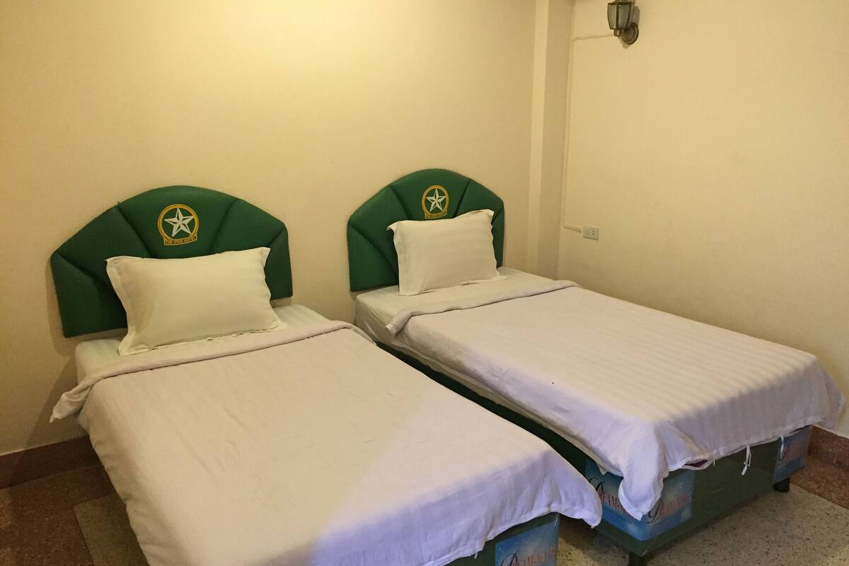 Two single beds with green headboards and white bedding in a room with a simple, clean design.