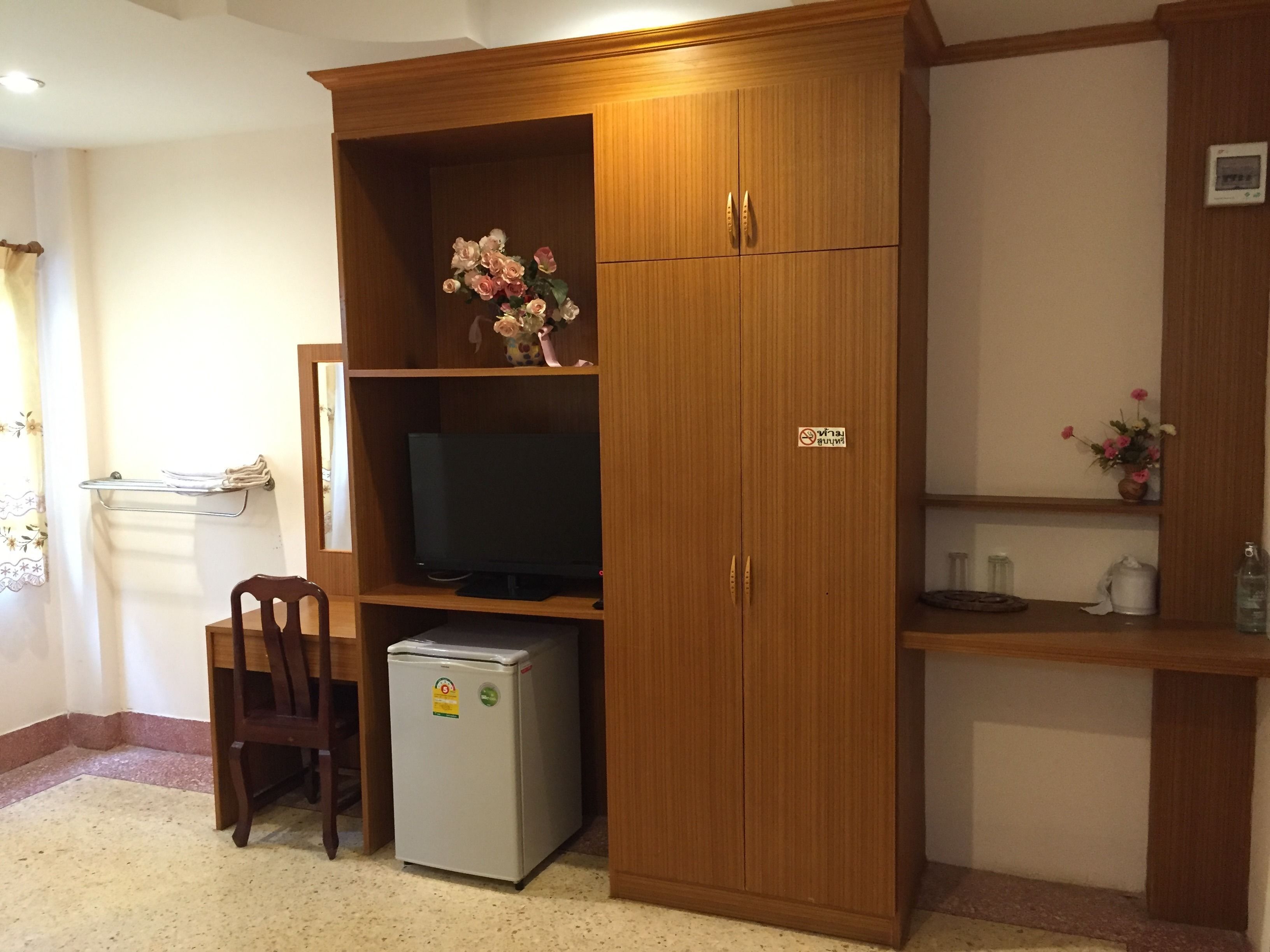 A compact room with a wooden cabinet containing a television, a small refrigerator, and a shelf with a vase of flowers.