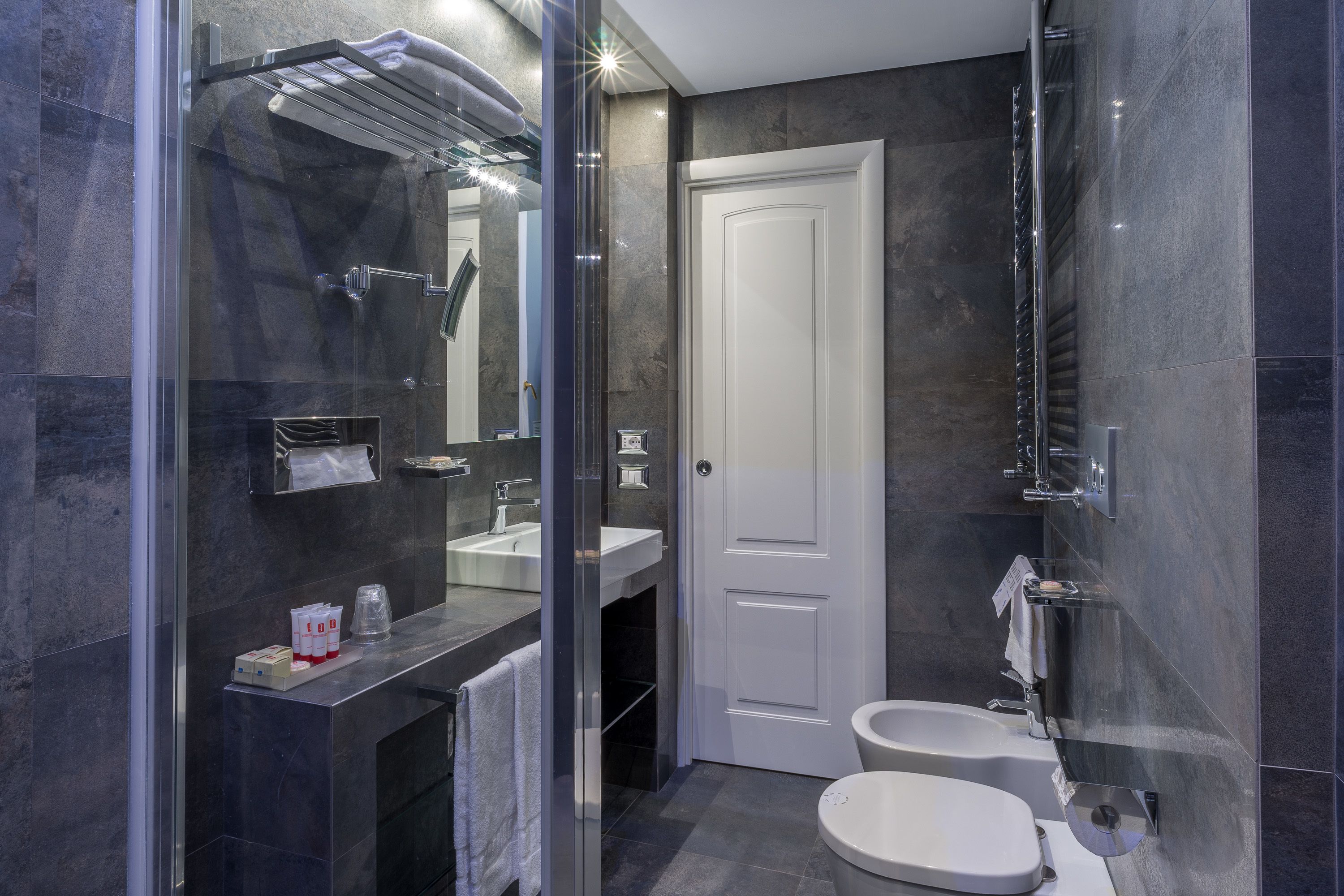 Un baño moderno con cabina de ducha de vidrio, dos lavamanos y una puerta blanca.