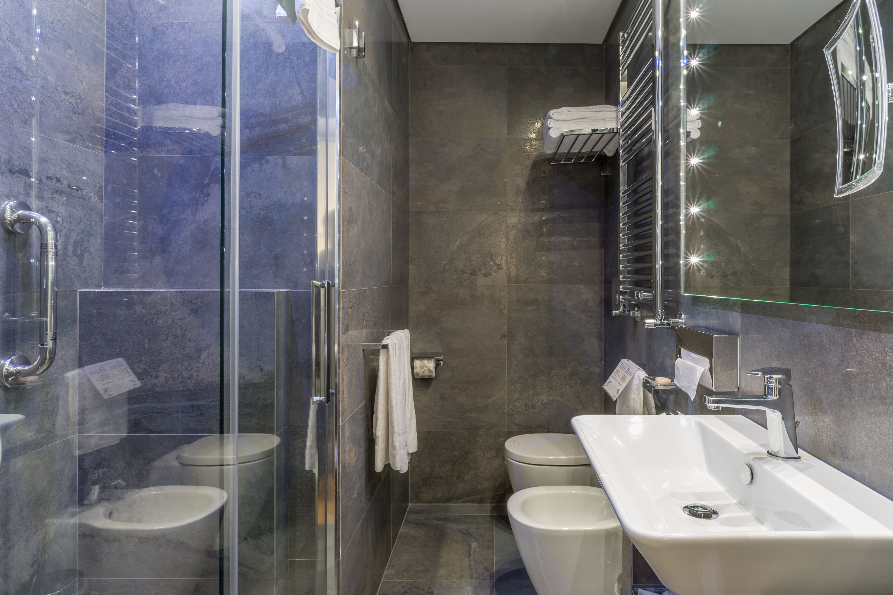 A modern bathroom with a glass-enclosed shower, a large sink, and two toilets.