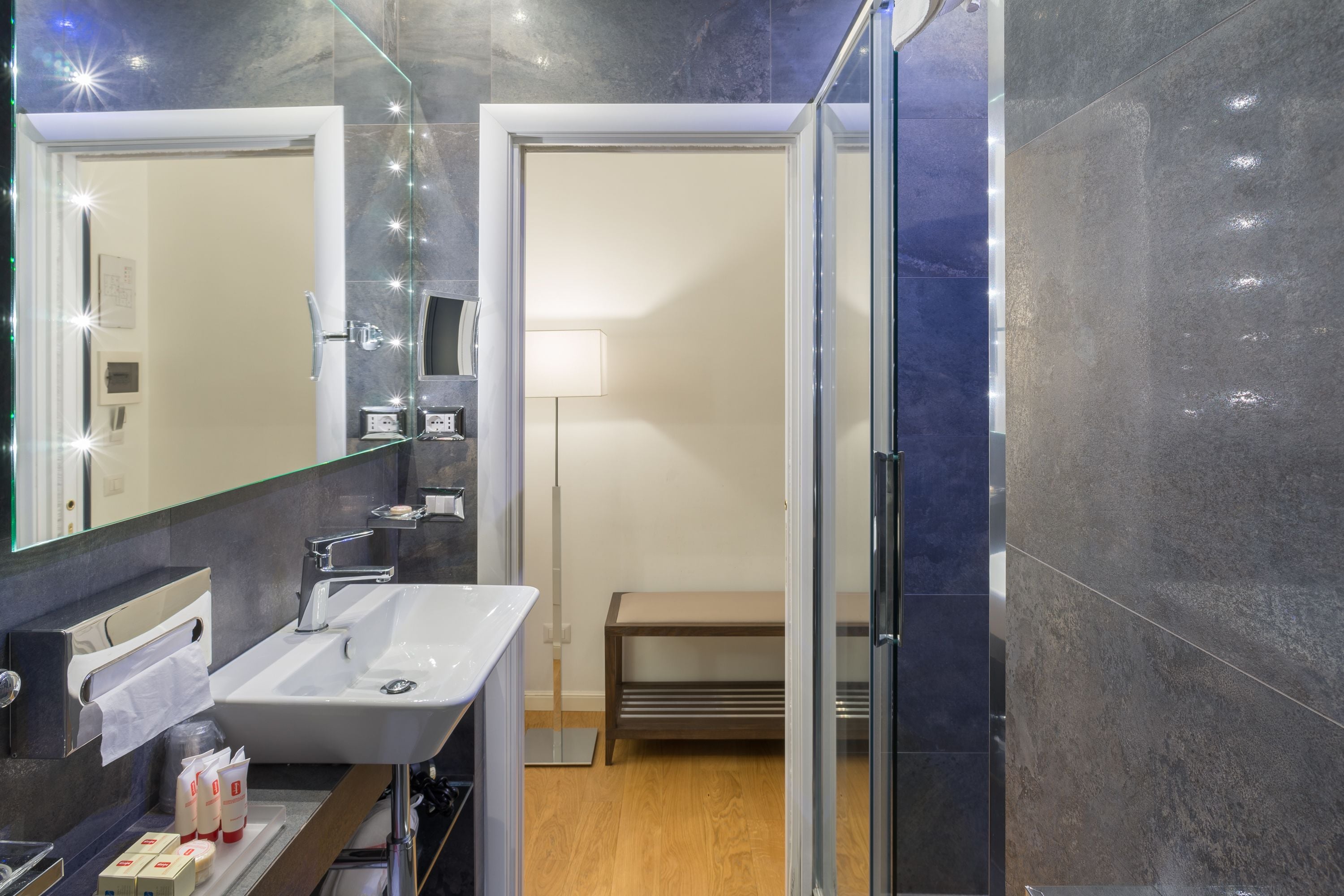 A modern bathroom with a large mirror, a sink, and a bench.